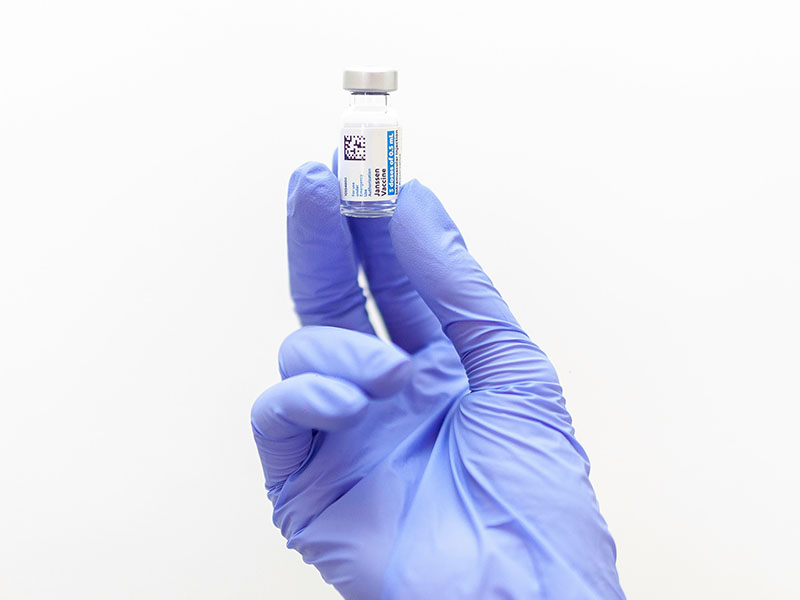 One hand with a blue glove holing a vaccine.