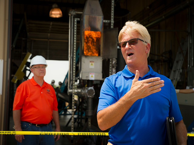 A man in a blue shirt giving a lecture in front of a machine. A man in a blue shirt giving a lecture in front of a machine.